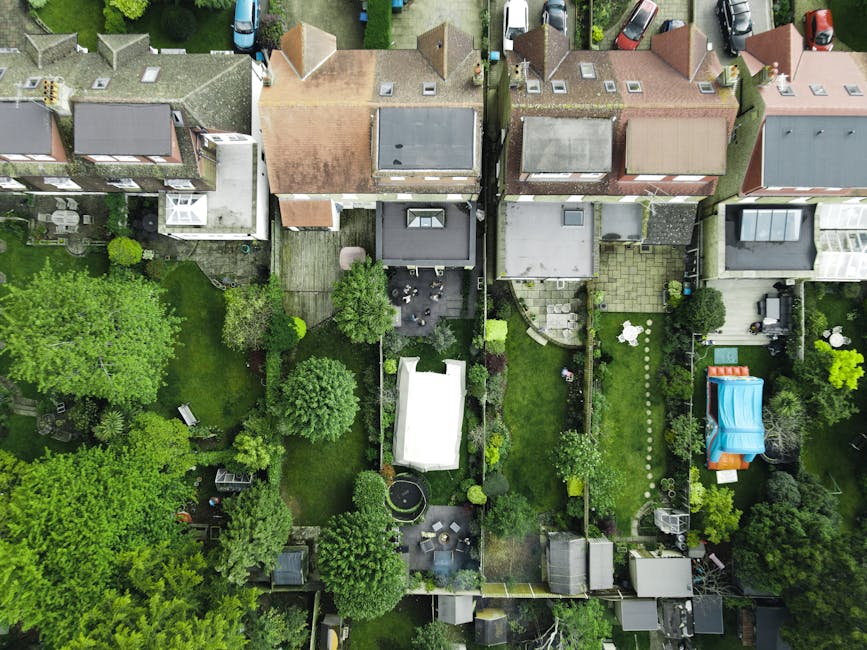 A neatly maintained garden featuring a well-trimmed lush green lawn with freshly cut grass, bordered by garden beds filled with a variety of leafy shrubs and flowering plants. In the background, tall 